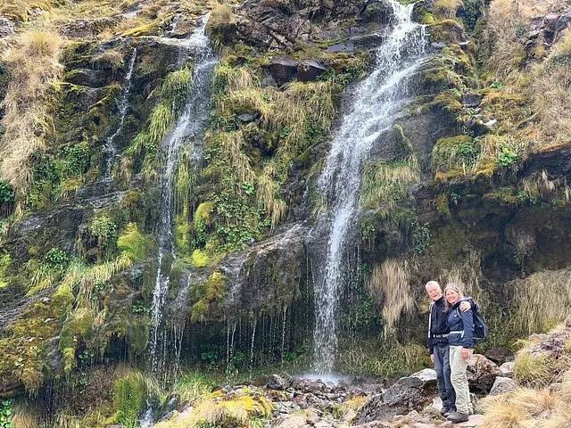 Couple posant devant une cascade sur une falaise rocheuse couverte de mousse.