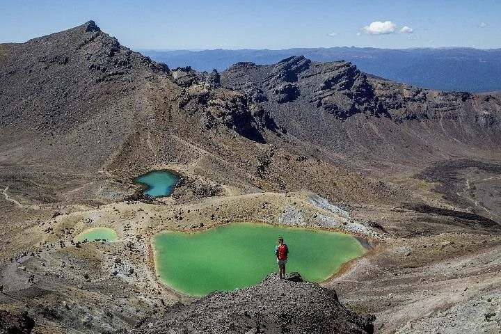 Senderista de pie sobre lagos volcánicos de un verde vibrante en un paisaje montañoso escarpado.