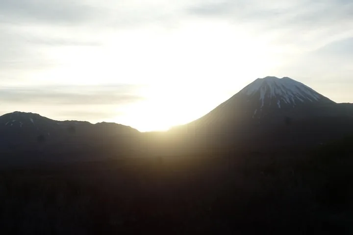 Zon die ondergaat of opkomt achter een besneeuwde vulkanische piek in silhouet.