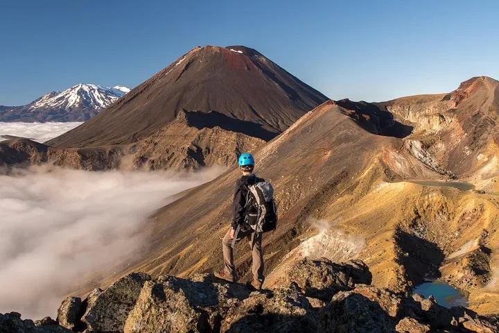 Randonneur debout sur une crête, contemplant les nuages et les pics volcaniques.