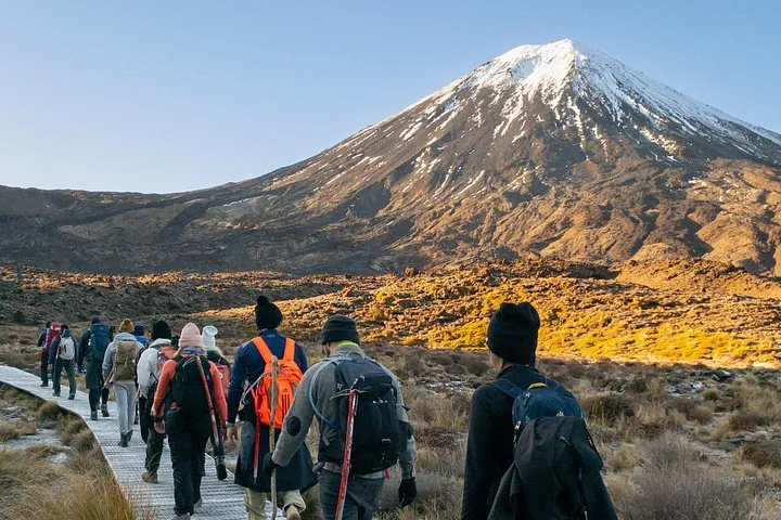 Senderistas caminando por una pasarela hacia el monte Ngauruhoe cubierto de nieve.