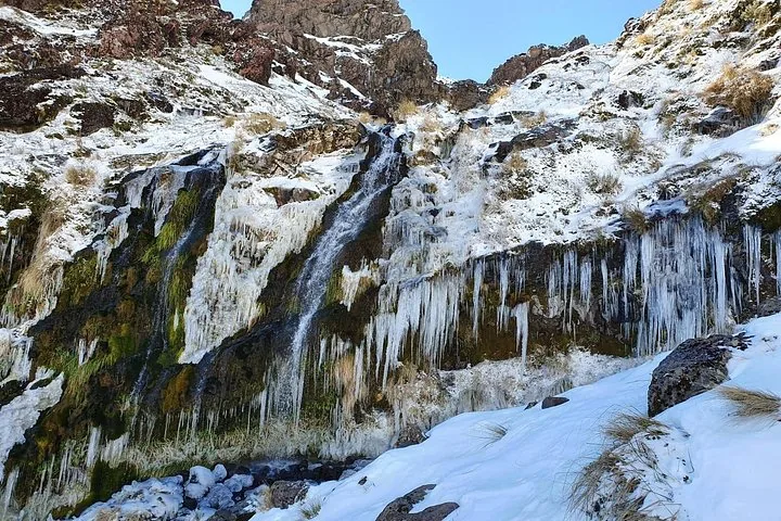 Teilweise gefrorener Wasserfall, der über eine felsige Klippe mit Schnee und Eiszapfen herabstürzt.